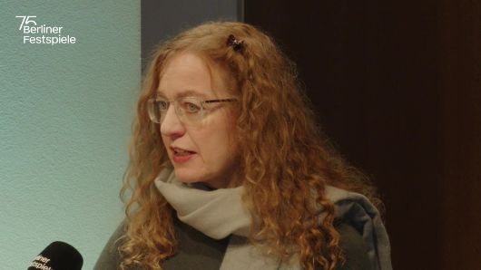 Alexandra Kedves spricht in ein Mikrofon und gestikuliert mit seiner linken Hand.