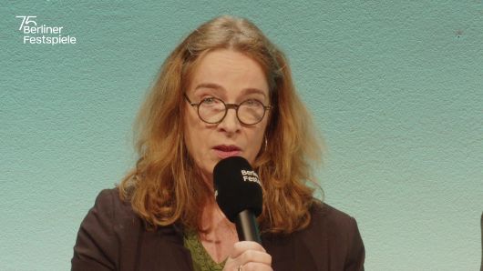 Sabine Leucht spricht in ein Mikrofon und gestikuliert mit seiner linken Hand