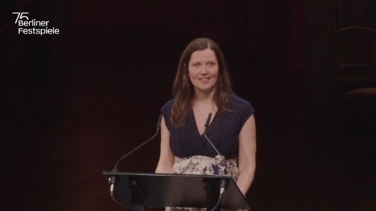 Nora Hertlein-Hull, the director of the Theatertreffen, is standing at a lectern.