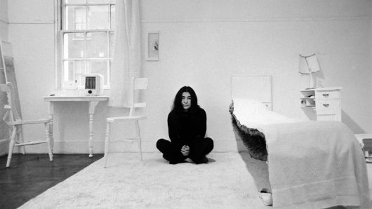 Black and white portrait of Yoko Ono sitting in her installation "HALF-A-ROOM" as part of the exhibition "HALF-A-WIND SHOW", Lisson Gallery, London, 1967.