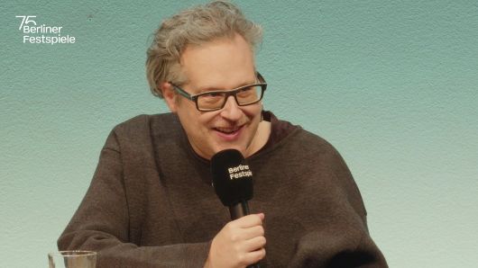 Falk Schreiber spricht in ein Mikrofon und gestikuliert mit seiner linken Hand