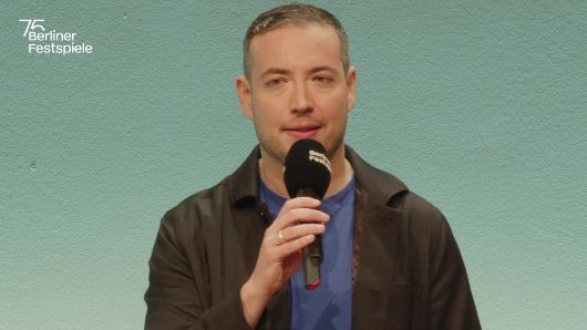 Martin Thomas Pesl spricht in ein Mikrofon und gestikuliert mit seiner linken Hand