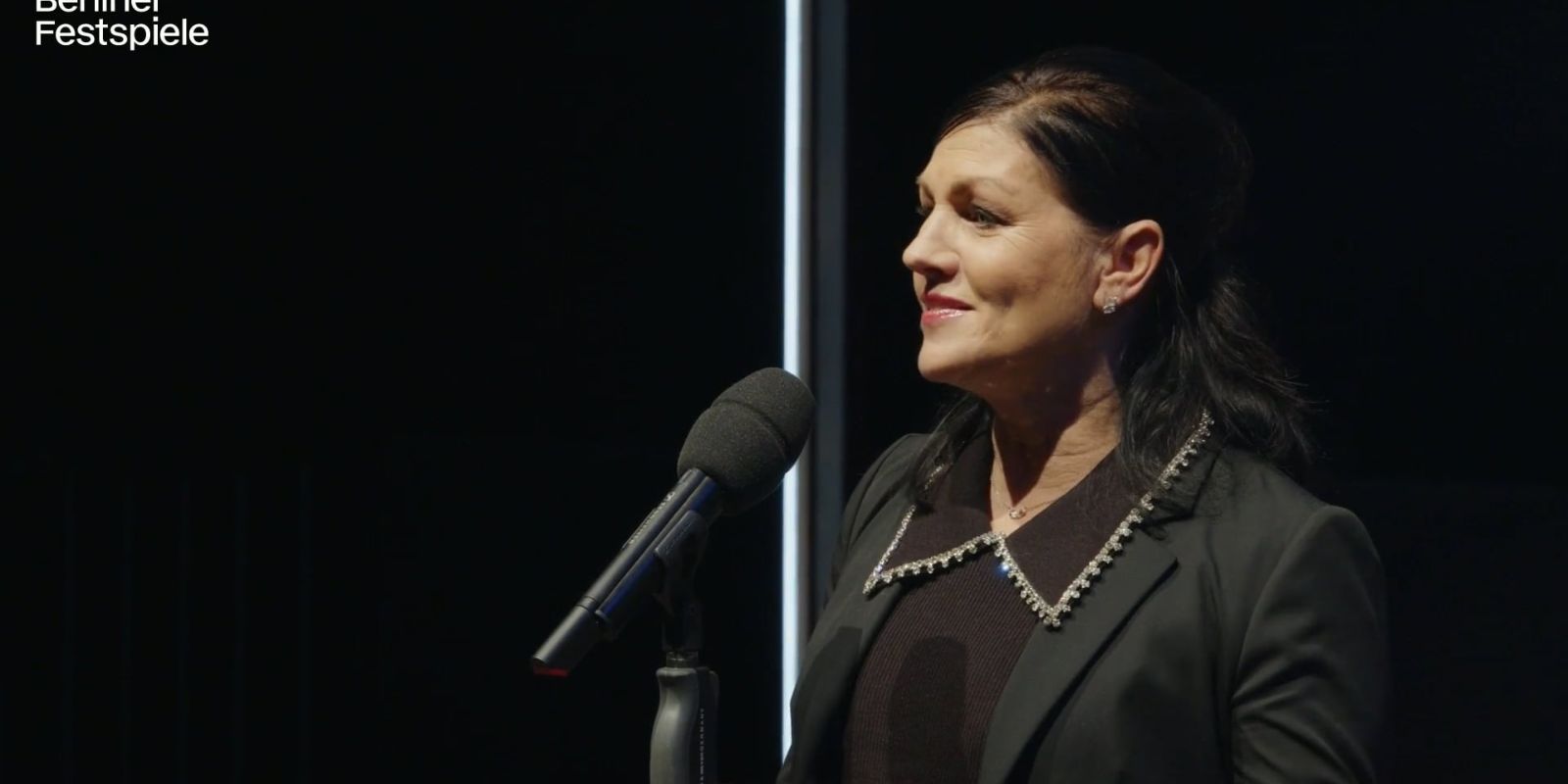 A person can be seen in profile with a microphone in front of them.