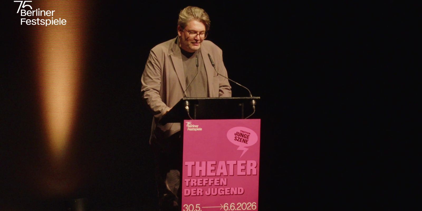 Person at lectern with microphones reading, dark background