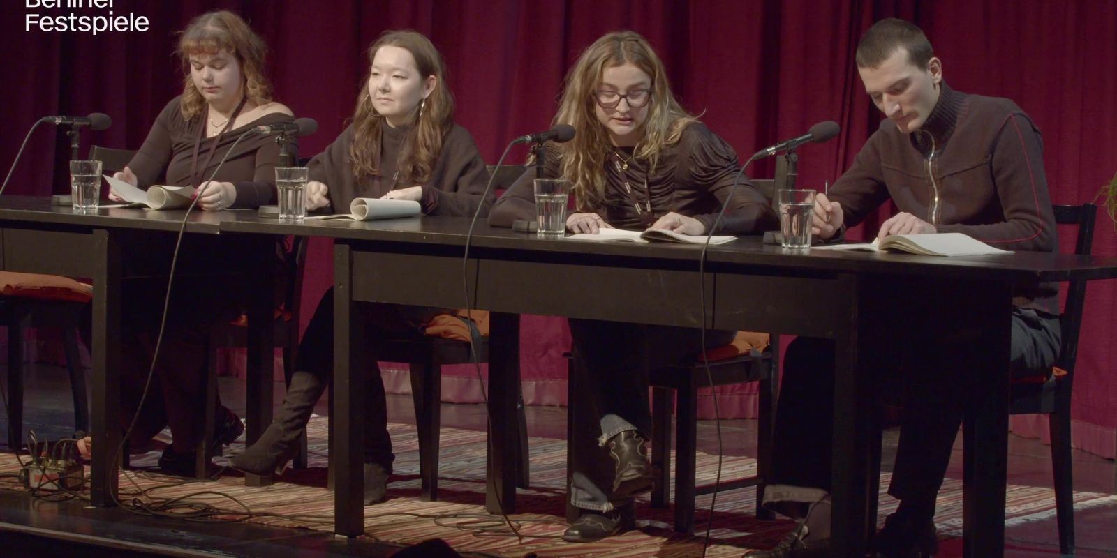 Four people sit next to each other at a table with microphones.