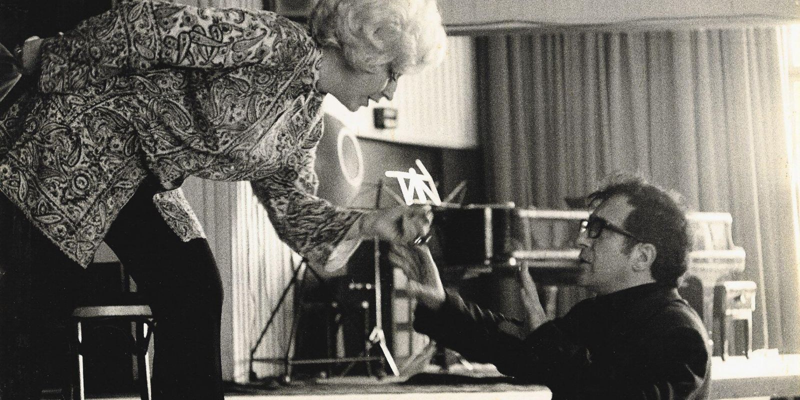 Der Komponist und die Sängerin diskutieren während einer Probe am Bühnenrand. Auf der Fotografie in schwarz-weiß steht sie auf der Bühne, beugt sich herunter, er macht eine beruhigende Geste. 