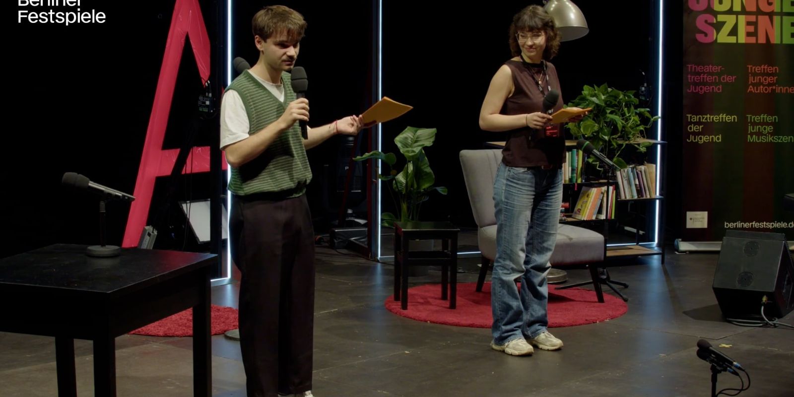 Two people are standing on a stage holding a microphone.