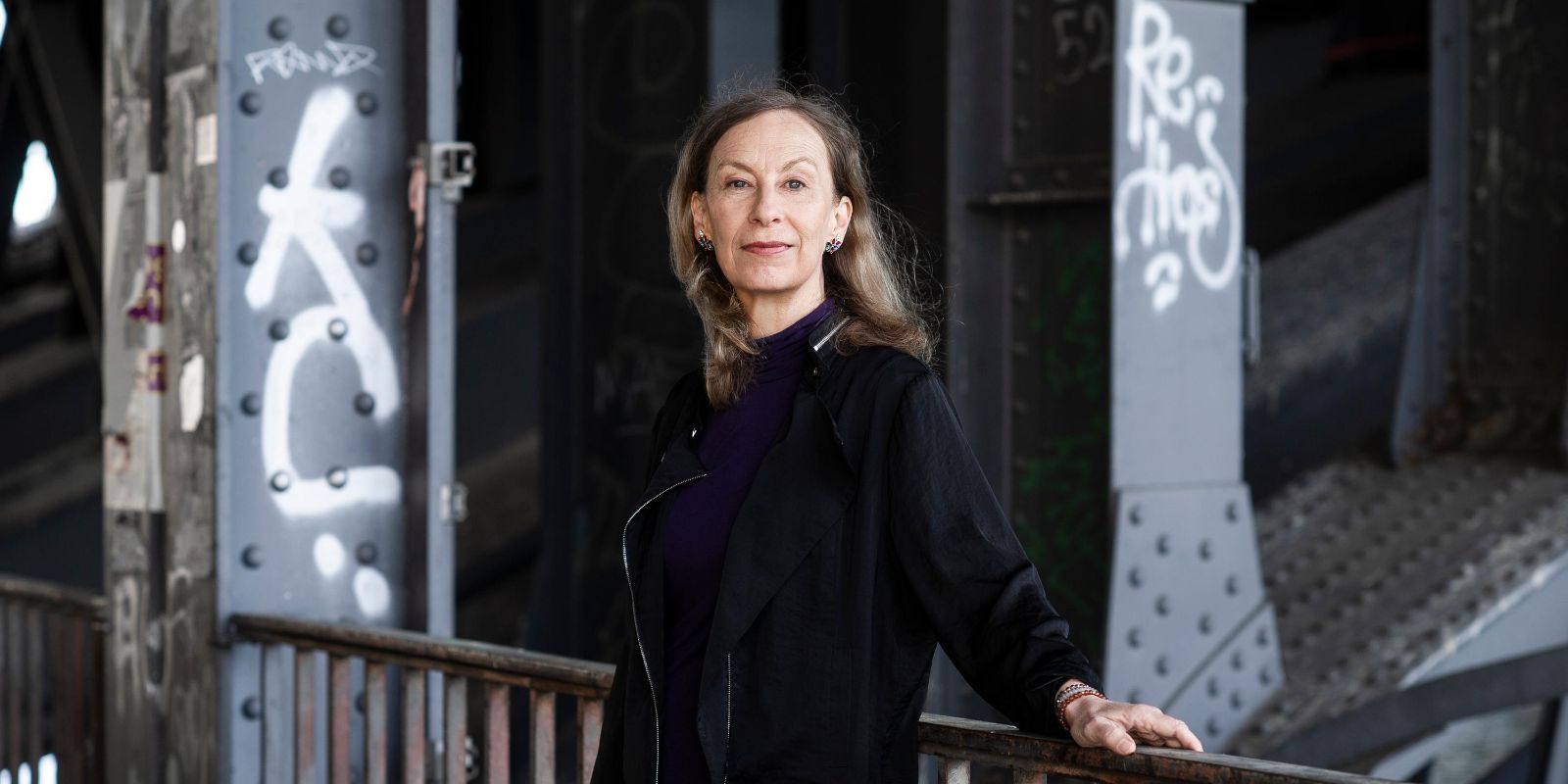 Person in dark clothing stands by a railing in front of a graffiti-covered wall.