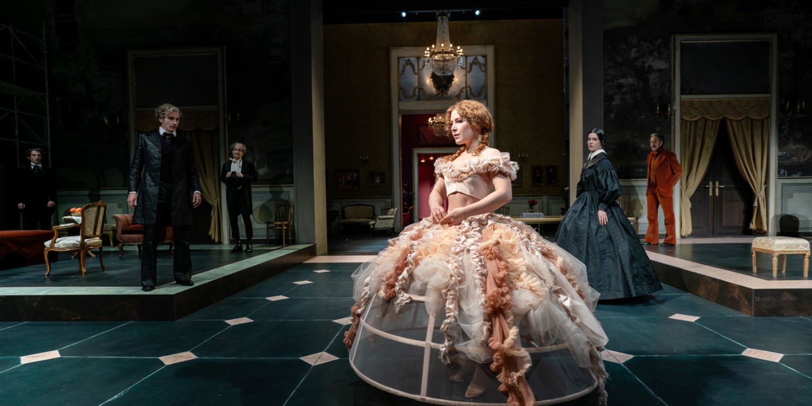 A young woman in a hoop skirt stands in a salon, with more people in historical costumes in the background