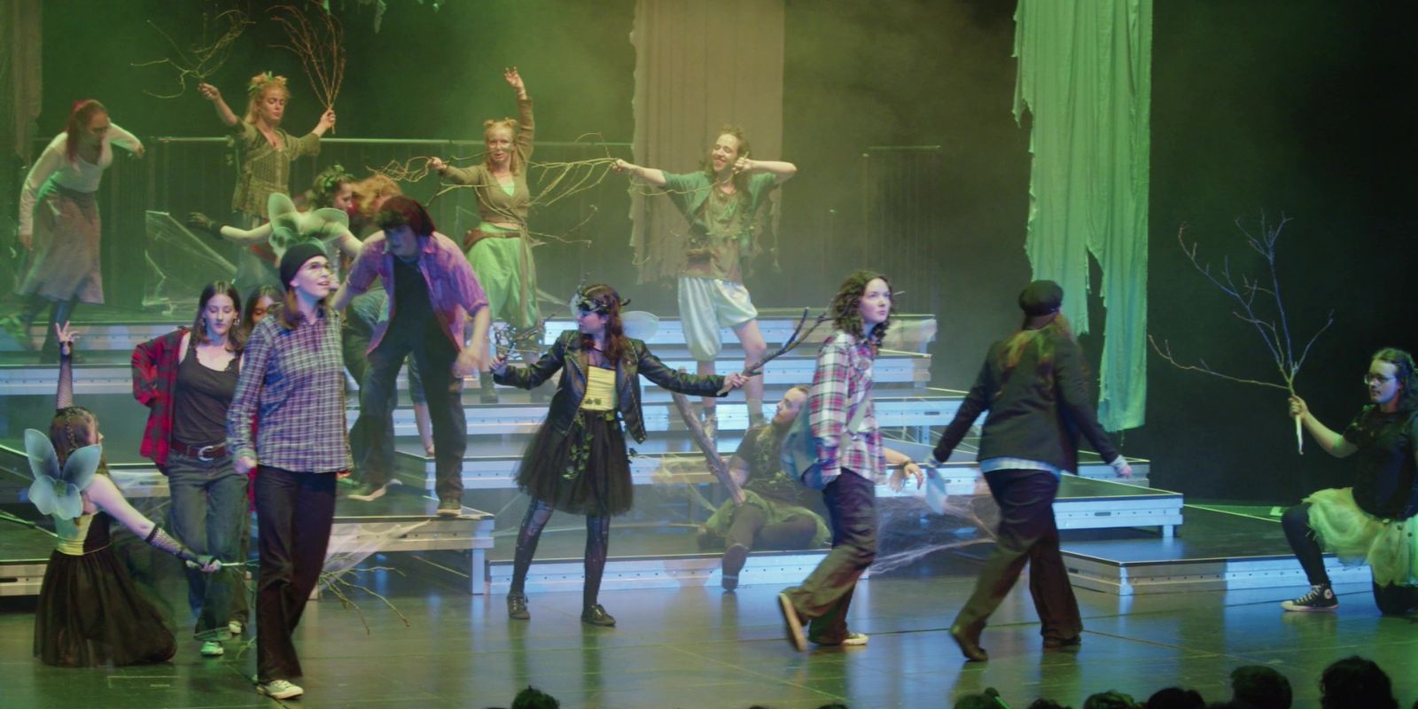 A group of young people holding branches in their hands dance on platforms on a stage.