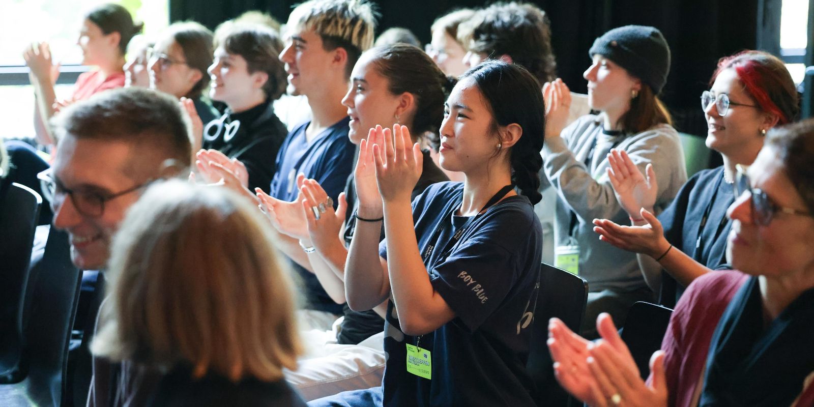 A group of young people sits on chairs and applauds.