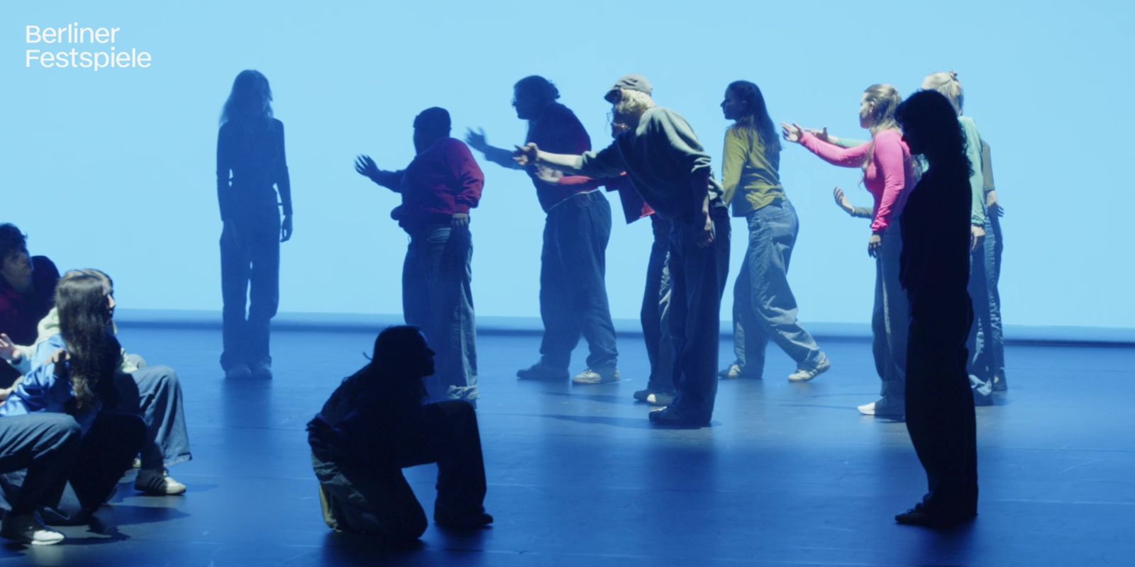 A group of people is moving across an empty, blue-lit stage.