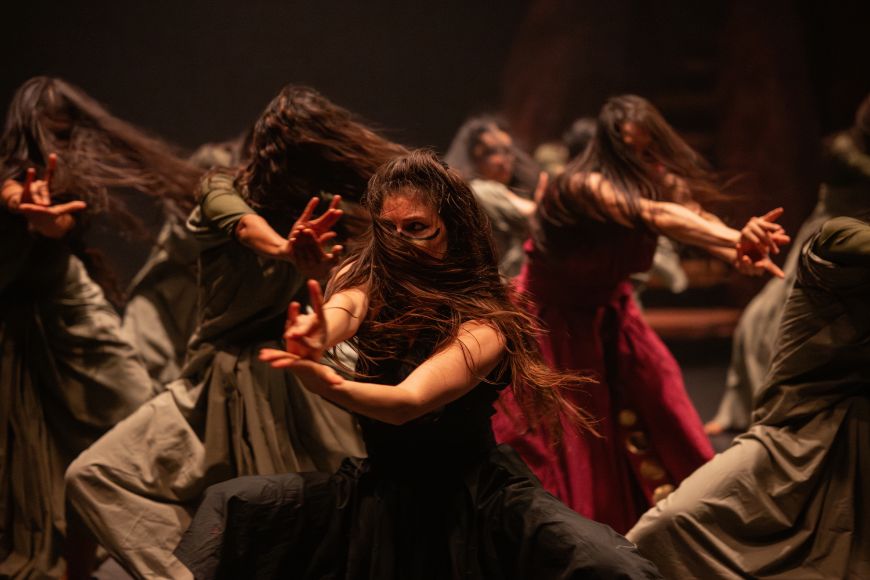 Dancers' long hair blows into their faces. Their hands form a fox, as if for a shadow play.