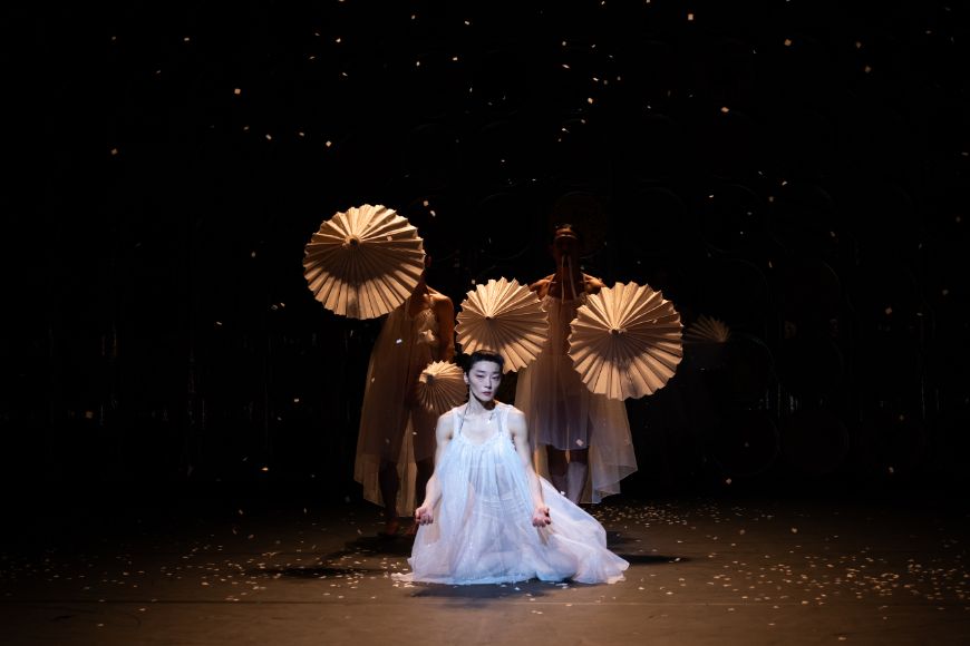 A dancer kneels on the floor in a transparent dress.