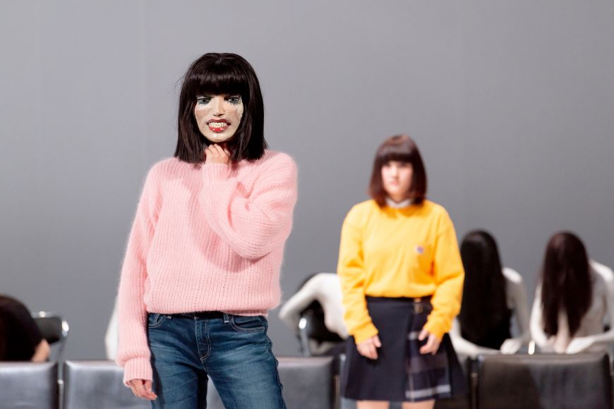 Ein Mensch trägt die Maske einer Puppe. Durch den großen Mund und die aufgemalten Augen wirkt sie unheimlich.