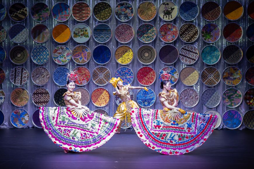 Two dancers each hold a huge, colourfully patterned fan in front of their bodies.