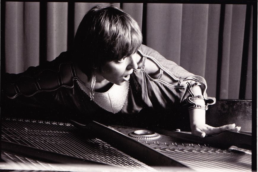 The artist rests her upper body on a grand piano during a concert.