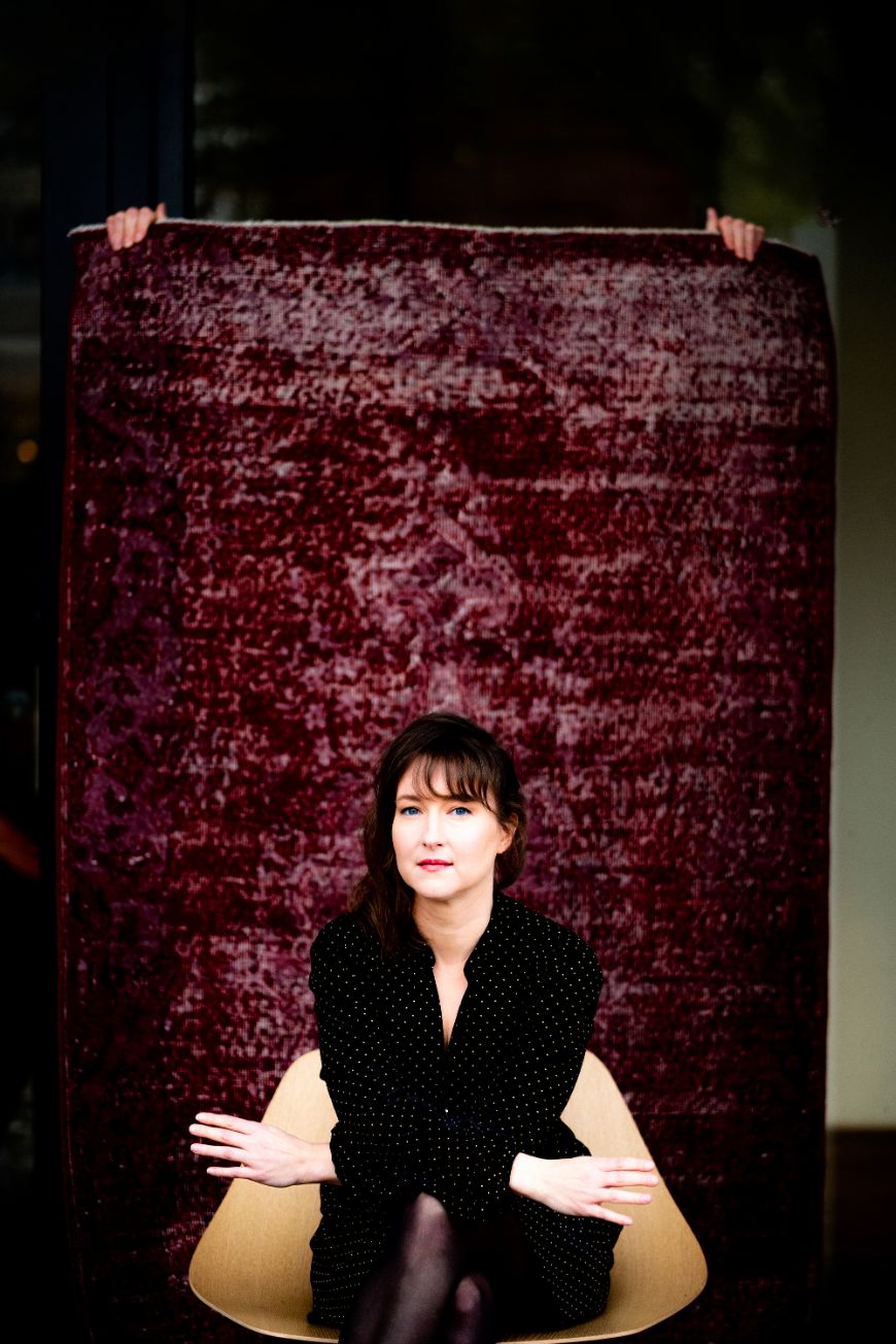 The composer Lisa Streich sits in front of a dark red-purple background.