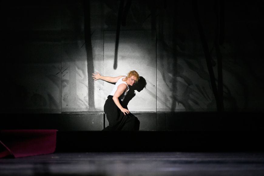 Eine Person im Spotlight vor einer besprühten Wand auf der Bühne