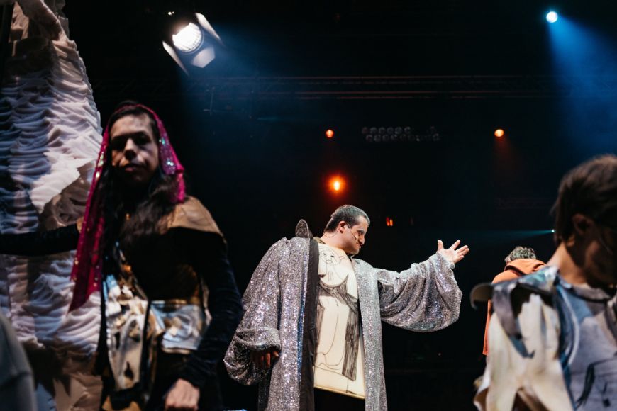 Eine Person in silber-glitzerndem Mantel neben mittelalterlich kostümierten Personen