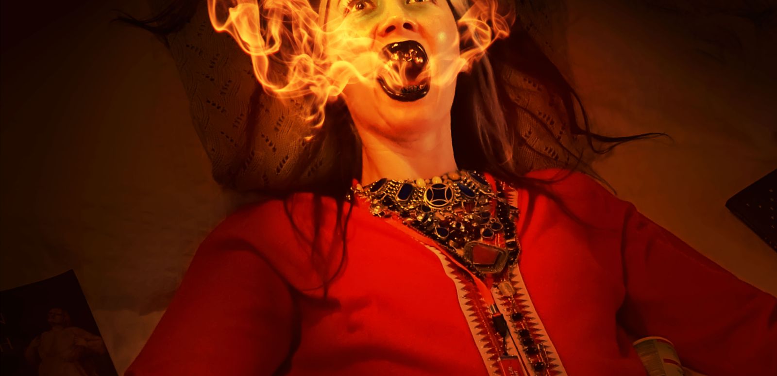 Porträt von Johanna Hedva liegend umgeben von Medikamenten und einem offenen Mund aus dem Feuerflammen kommen