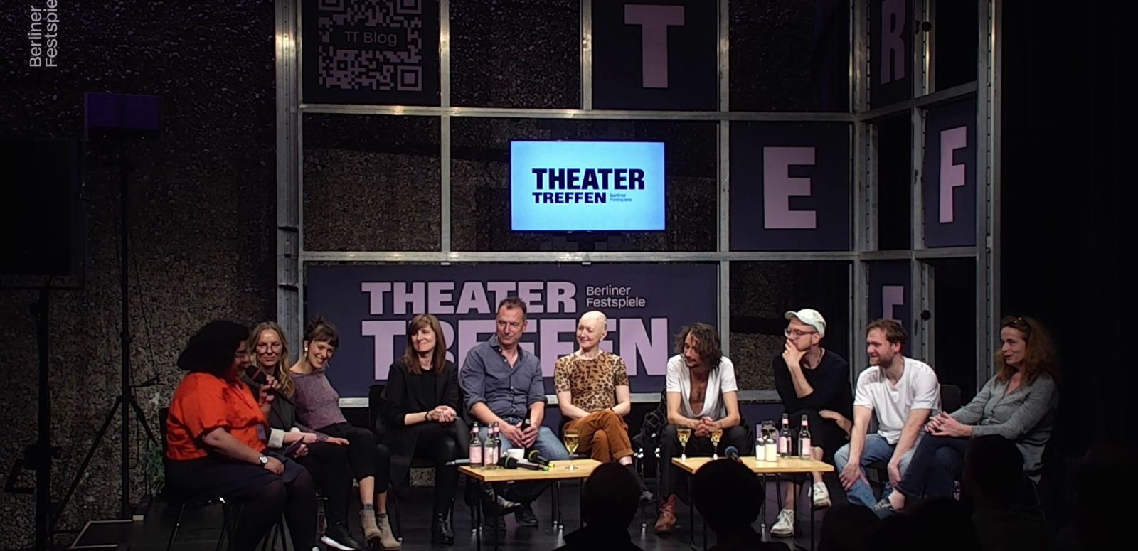 A group of 10 people discuss on a stage. 