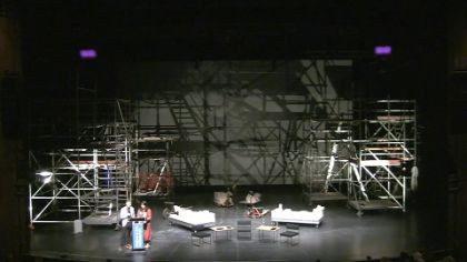 Meron Mendel und Saba-Nur Cheema stehen auf einer Bühne umgeben von dem gerüstartigen Bühnenbild des Stückes „House“.