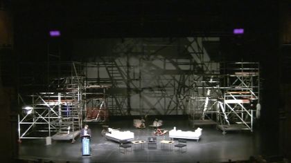 Yassin Musharbash stands on a stage surrounded by the scaffolding-like set of the play "House".