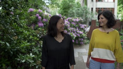 Liza Lim and Martina Seeber walk through a garden with blossoming flowers.